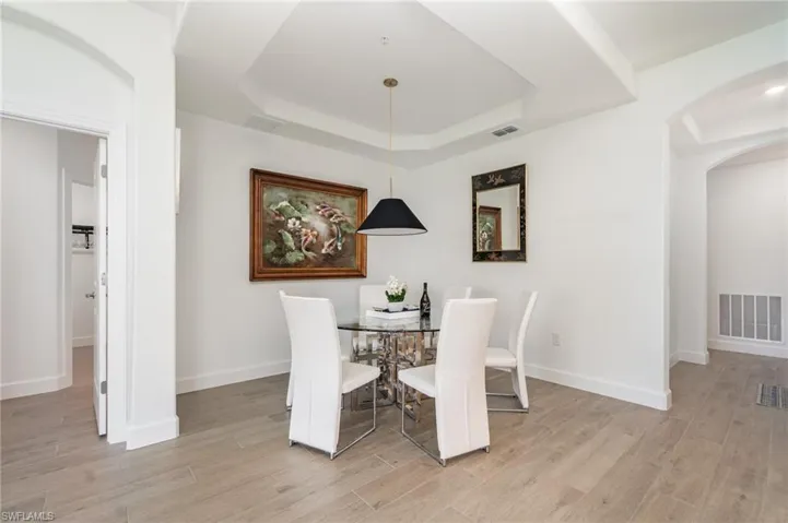 Dining room featuring arched walkways, light wood-style flooring, and a raised ceiling