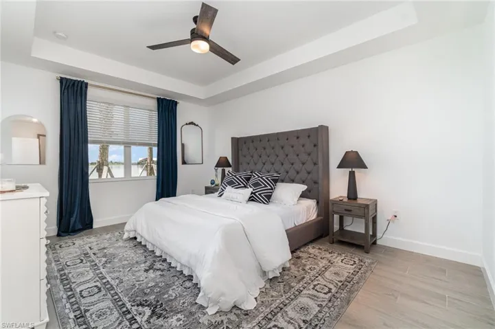 Bedroom with a raised ceiling, light wood finished floors, and a ceiling fan