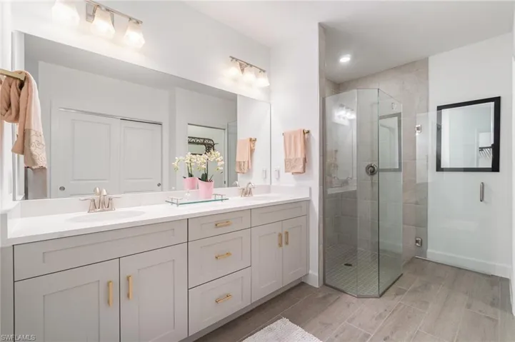Bathroom with double vanity, a stall shower, and wood finish floors