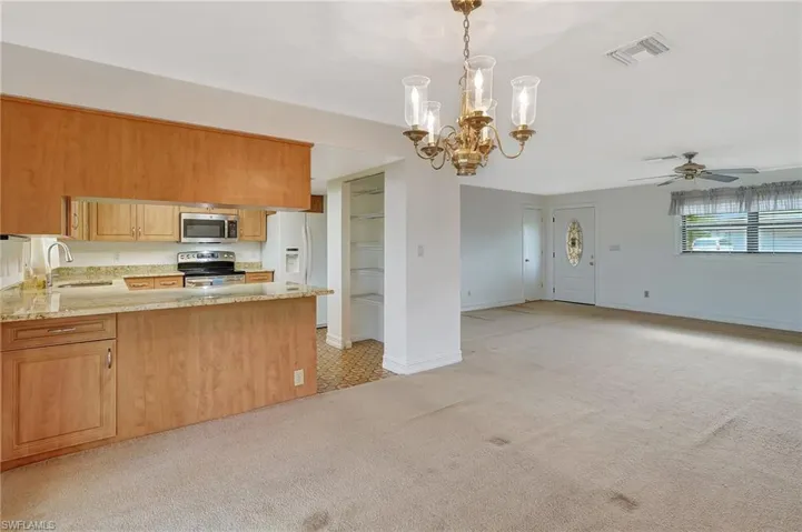 Kitchen featuring stainless steel microwave, a sink, range with electric stovetop, white fridge with ice dispenser, and light colored carpet