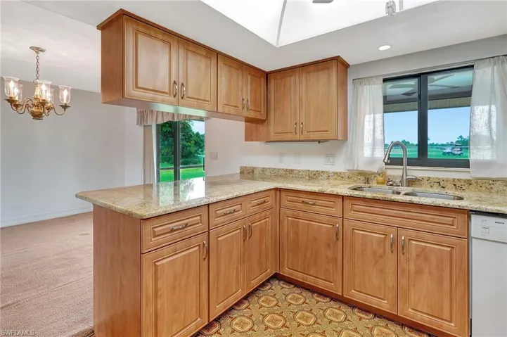 Kitchen with dishwasher, a sink, light stone counters, a peninsula, and healthy amount of natural light
