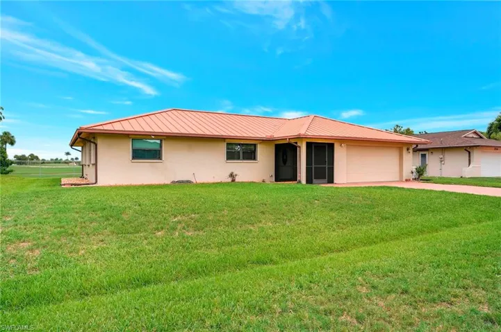 Single story home with stucco siding, a garage, concrete driveway, metal roof, and a front lawn