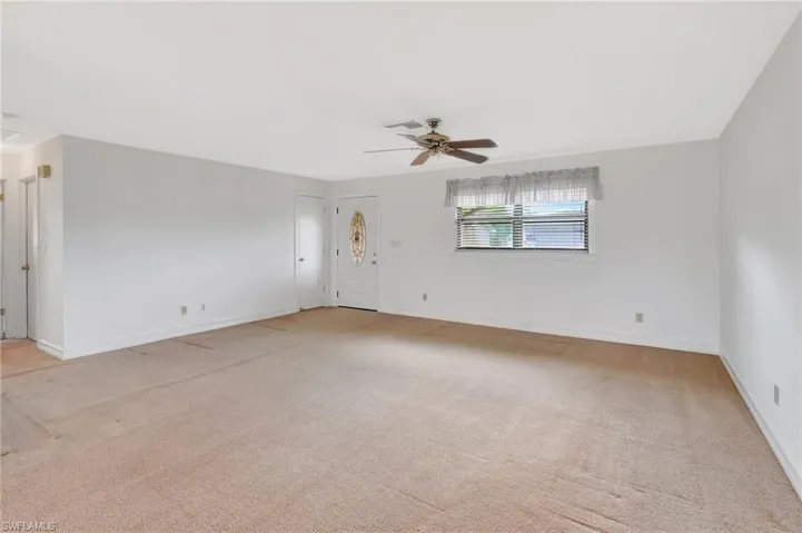 Empty room featuring light colored carpet, a ceiling fan, and baseboards