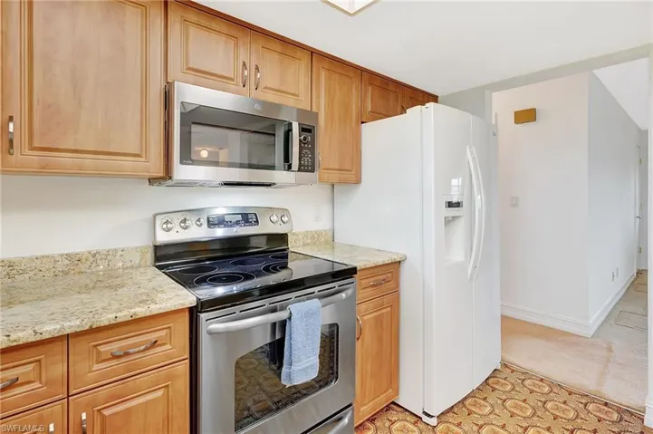 Kitchen with stainless steel appliances, light stone countertops, and light colored carpet