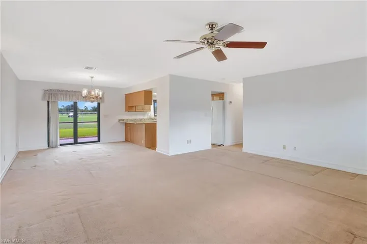 Unfurnished living room featuring a chandelier, baseboards, ceiling fan, and light colored carpet