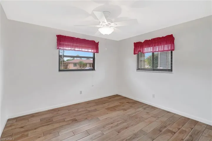 Empty room featuring plenty of natural light, wood finished floors, a ceiling fan, and baseboards