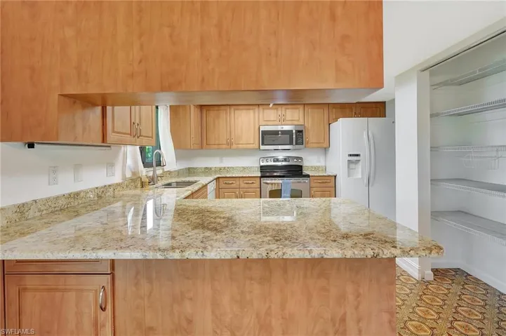 Kitchen with stainless steel appliances, a sink, light stone countertops, a peninsula, and brown cabinetry