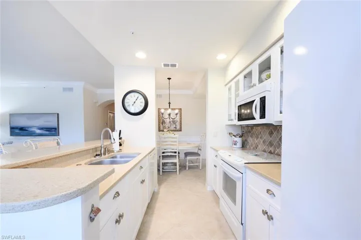 Kitchen with white cabinetry, white appliances, ornamental molding, decorative light fixtures, and light stone counters