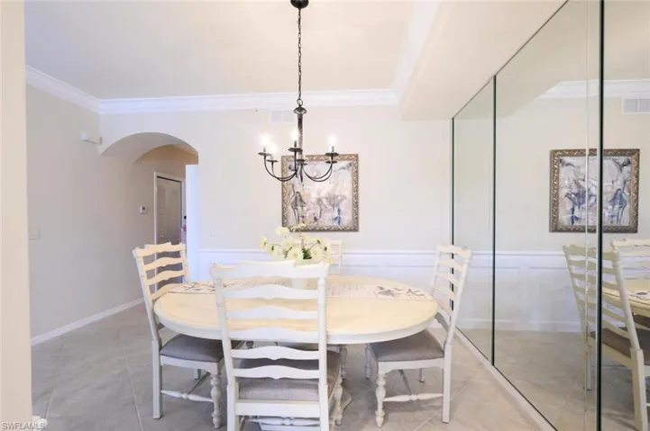 Dining area featuring ornamental molding, light tile patterned flooring, arched walkways, a chandelier, and a decorative wall