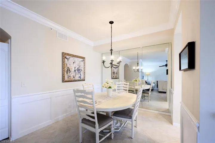 Dining space featuring crown molding, a chandelier, wainscoting, a decorative wall, and light tile patterned floors