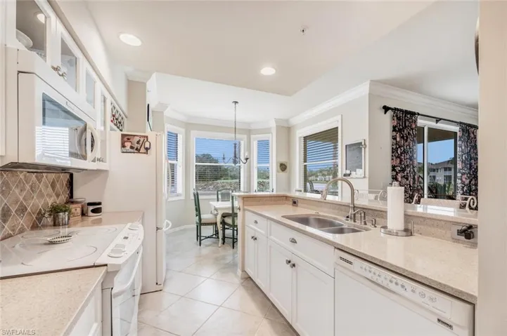 Kitchen with white cabinets, white appliances, glass insert cabinets, light stone countertops, and crown molding