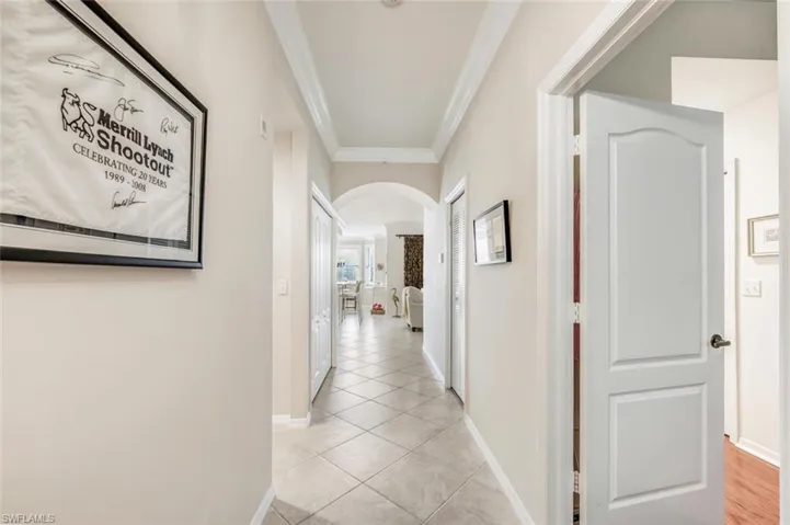 Hallway with arched walkways, ornamental molding, and light tile patterned flooring