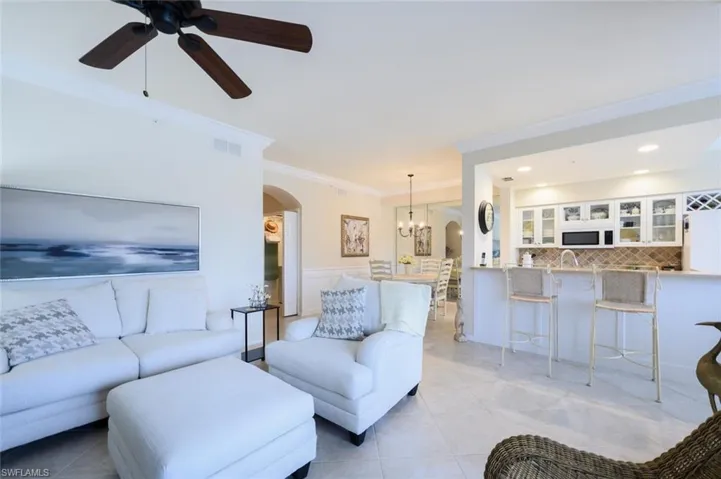 Living room with arched walkways, light tile patterned floors, ornamental molding, a chandelier, and ceiling fan