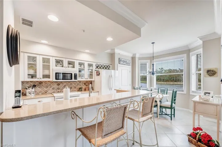 Kitchen with ornamental molding, a peninsula, a kitchen bar, white cabinets, and light stone counters