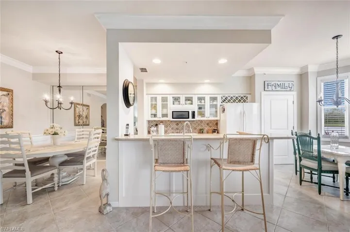 Kitchen featuring hanging light fixtures, a chandelier, glass insert cabinets, ornamental molding, and a breakfast bar