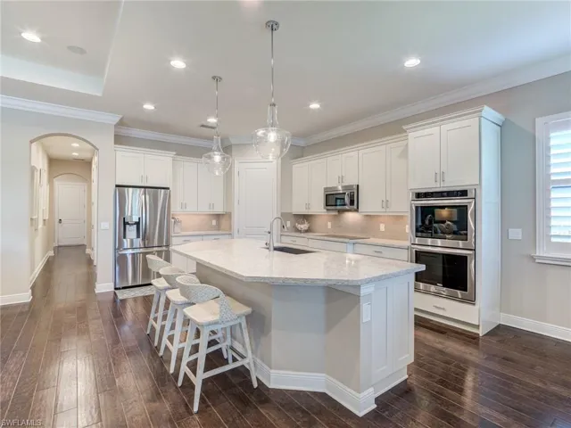 Kitchen with white cabinetry, stainless steel appliances, backsplash, arched walkways, and ornamental molding