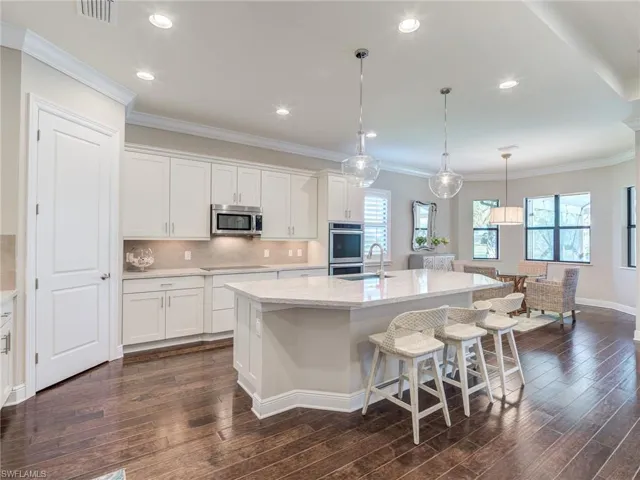 Kitchen with crown molding, tasteful backsplash, light stone counters, hanging light fixtures, and white cabinetry