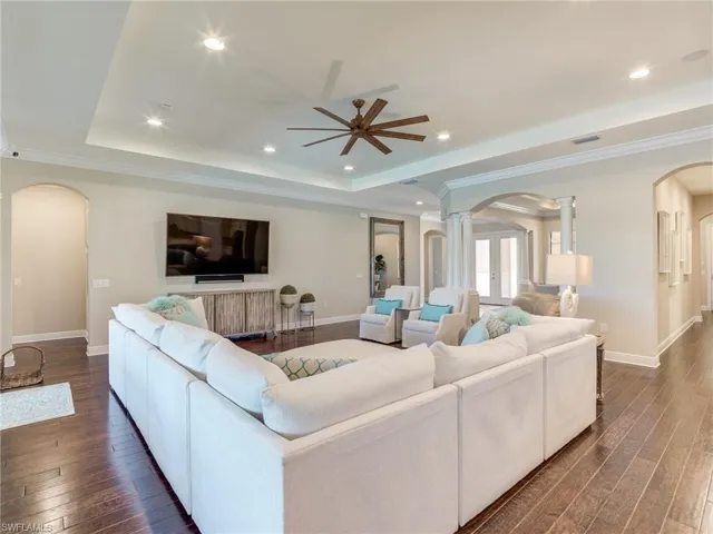 Living area with arched walkways, a tray ceiling, dark wood-style flooring, ceiling fan, and recessed lighting