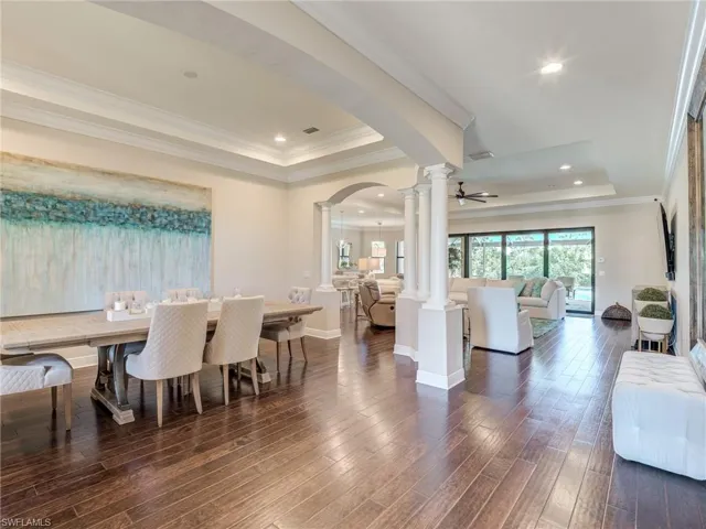 Dining space with a tray ceiling, decorative columns, arched walkways, crown molding, and dark wood-type flooring