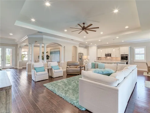 Living room featuring a raised ceiling, arched walkways, crown molding, dark wood finished floors, and recessed lighting