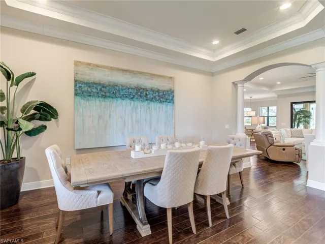 Dining area with a raised ceiling, crown molding, arched walkways, dark wood-style floors, and decorative columns