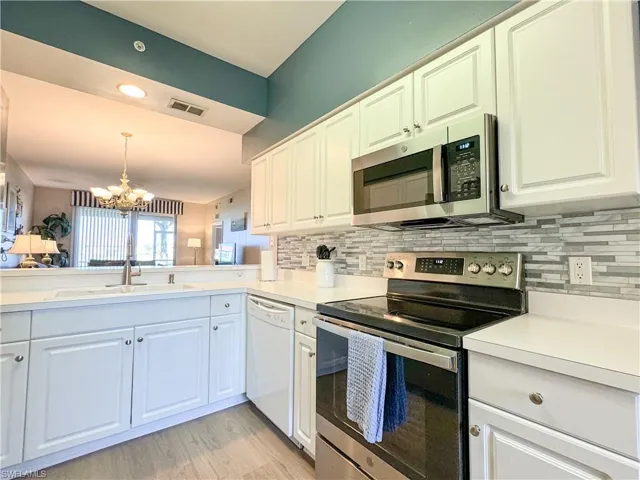 Kitchen featuring appliances with stainless steel finishes, tasteful backsplash, light wood-type flooring, and an inviting chandelier