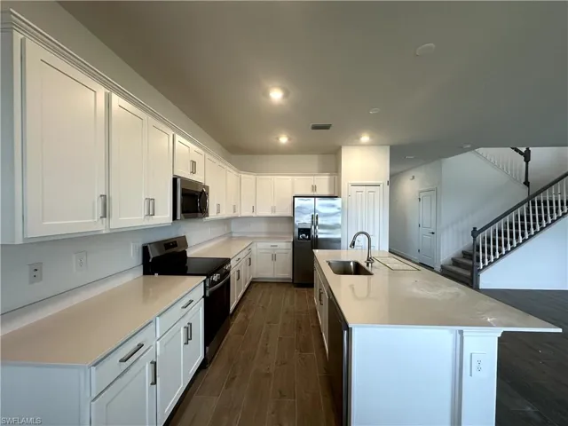 Kitchen with stainless steel appliances, dark hardwood / wood-style flooring, white cabinets, sink, and a kitchen island with sink