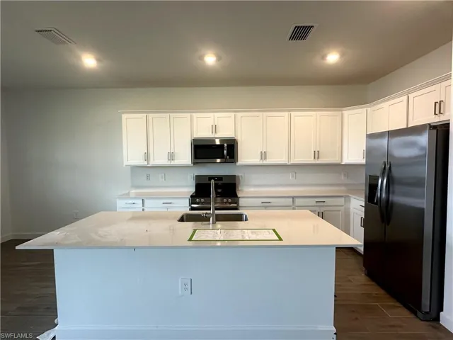 Kitchen with white cabinetry, dark hardwood / wood-style flooring, appliances with stainless steel finishes, and a center island with sink