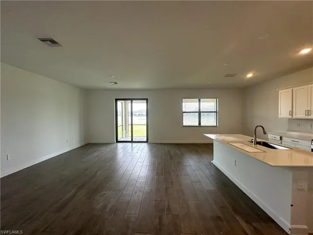Kitchen featuring sink, dark hardwood / wood-style floors, a center island with sink, and white cabinetry