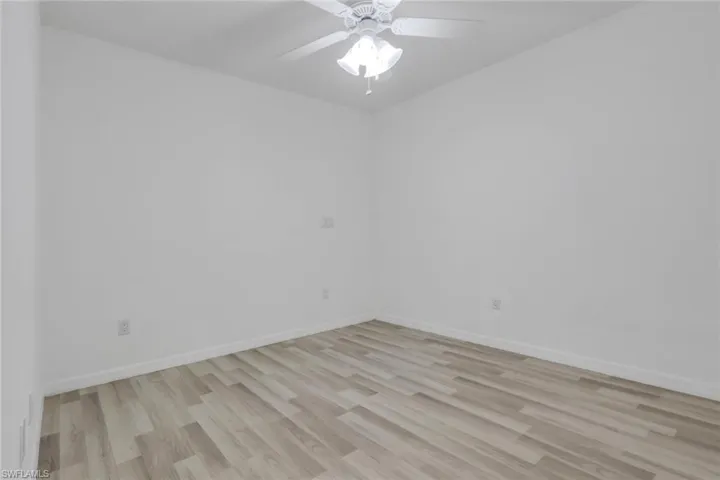 Room featuring light wood-finish flooring, white walls, white baseboards, and a white ceiling fan with integrated lighting