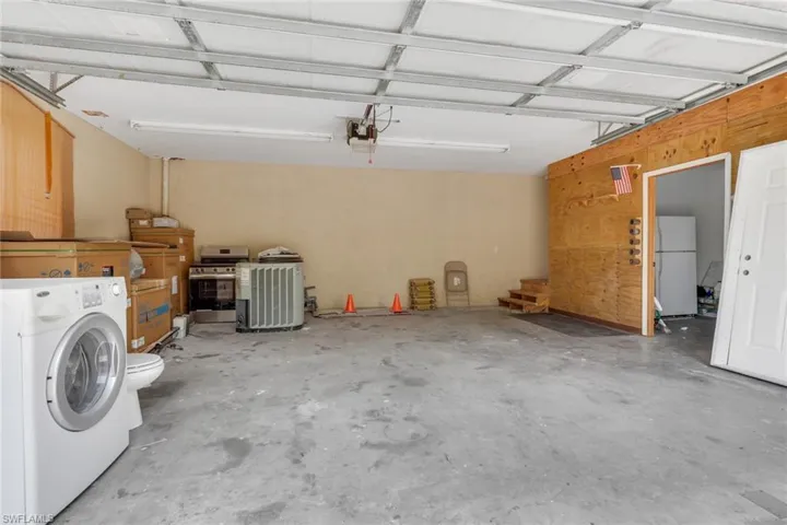 Spacious garage with exposed beam ceiling, concrete flooring, and a dedicated utility area