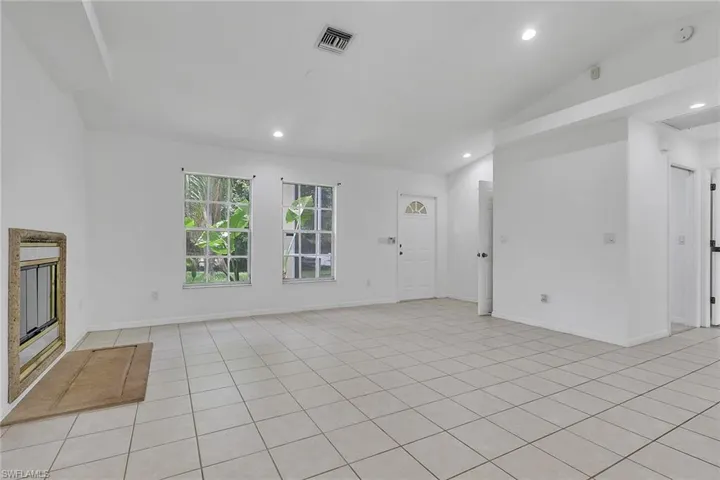 Spacious room featuring light-toned tile flooring, white walls, and a vaulted ceiling