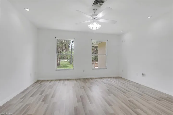 Spacious room featuring wood-finish flooring, two windows, recessed lighting, a ceiling fan with light fixture, and white painted walls