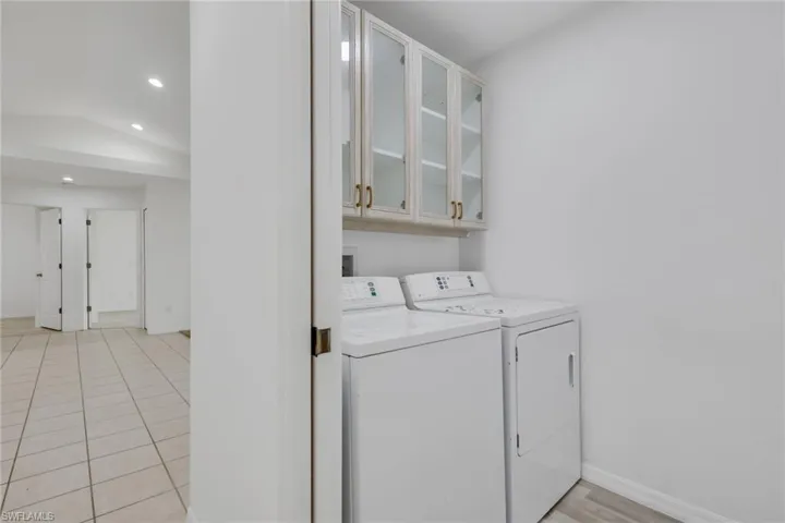 Laundry area featuring white walls, overhead cabinetry with glass inserts and brass-toned hardware, and a tile flooring