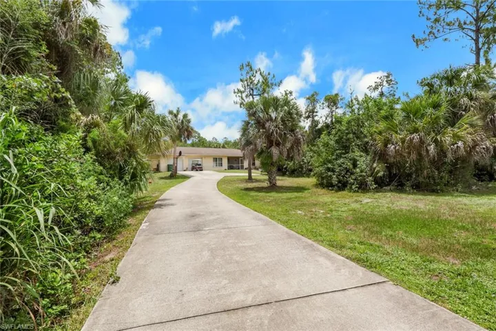 Long paved driveway leading to a single-story residence with a beige exterior