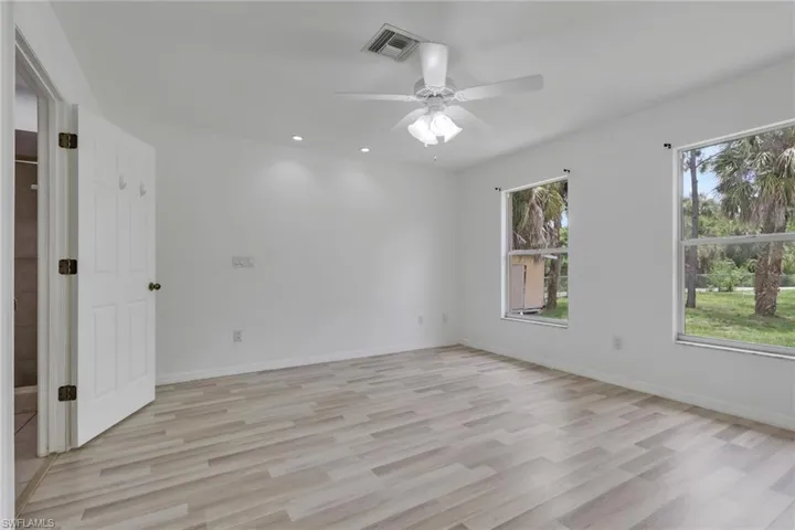Spacious room featuring wood-finish flooring, two large windows, a ceiling fan with integrated lighting, and recessed ceiling lights