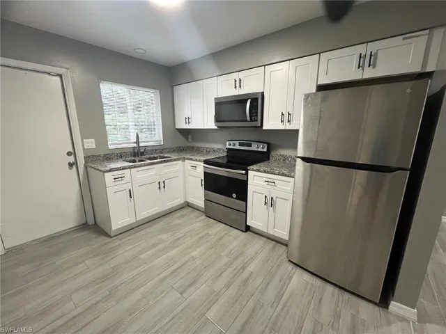 Kitchen featuring white cabinets, stone countertops, stainless steel appliances, and sink