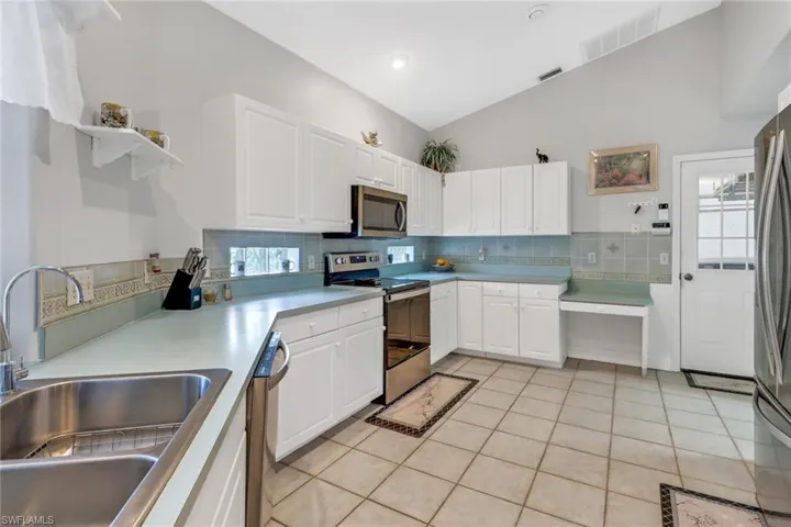 Kitchen with tasteful backsplash, white cabinets, sink, appliances with stainless steel finishes, and light tile patterned floors