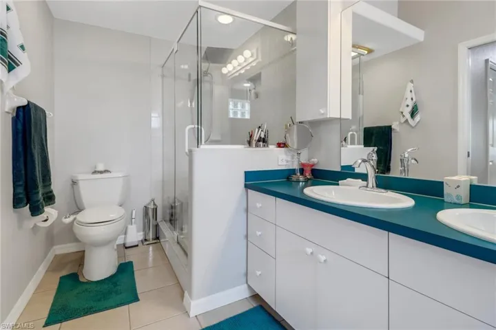 Bathroom with tile patterned flooring, a shower with shower door, toilet, and dual bowl vanity