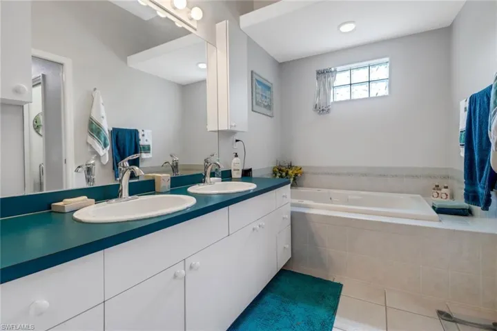 Bathroom featuring a relaxing tiled tub, tile patterned flooring, and dual bowl vanity