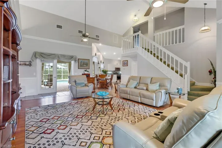 Living room with ceiling fan, hardwood / wood-style flooring, crown molding, and high vaulted ceiling