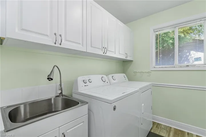 Laundry area featuring wood finished floors, a sink, baseboards, independent washer and dryer, and cabinet space