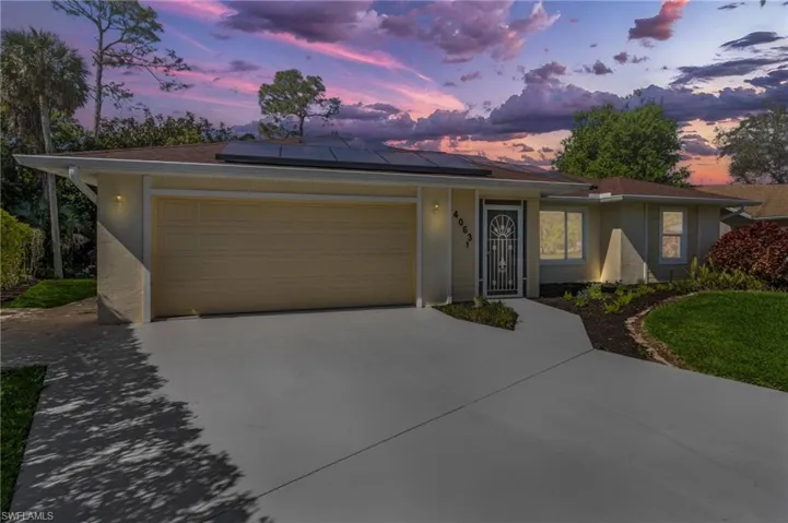 Ranch-style home featuring roof mounted solar panels, driveway, an attached garage, and stucco siding