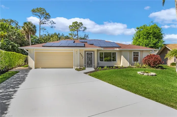 Ranch-style home featuring a garage, a front lawn, concrete driveway, solar panels, and stucco siding