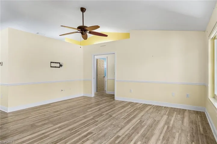 Unfurnished great room with vaulted ceiling, wood finished floors, a ceiling fan, and baseboards