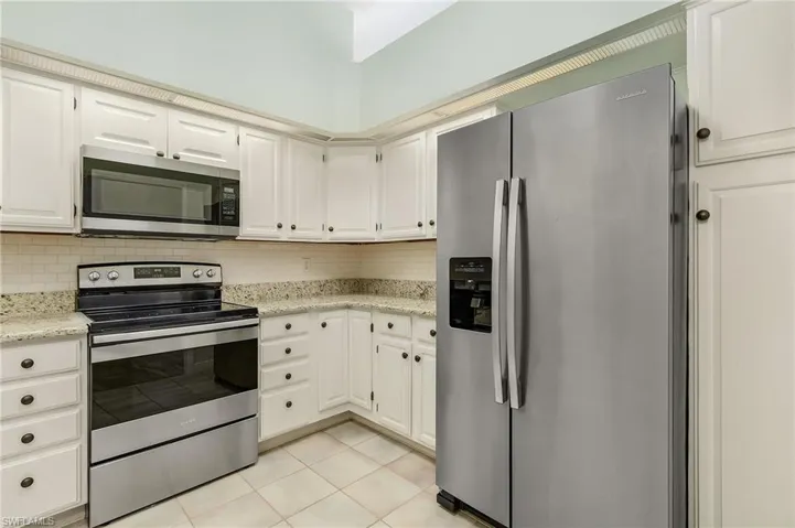 Kitchen with light stone counters, light tile patterned flooring, white cabinetry, appliances with stainless steel finishes, and decorative backsplash