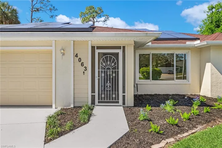 Doorway to property with a garage, roof mounted solar panels, and stucco siding