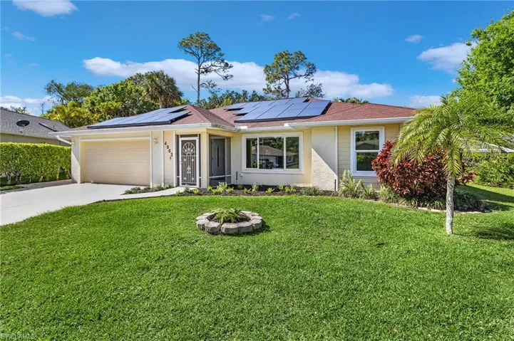 Single story home featuring a garage, a front yard, concrete driveway, roof mounted solar panels, and stucco siding
