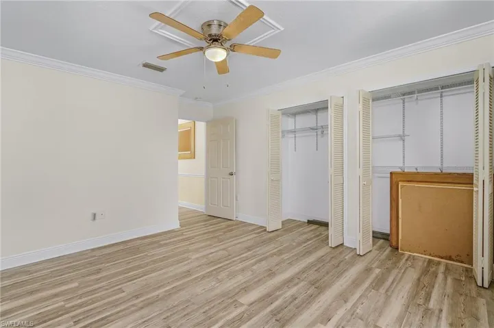 Bedroom 2 featuring light wood-style flooring, visible vents, baseboards, ornamental molding, and two closets