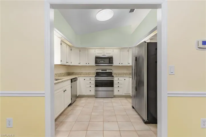 Kitchen featuring light tile patterned floors, white cabinets, decorative backsplash, and stainless steel appliances